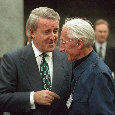 Brian Mulroney and Jacques Cousteau stand close to one another, talking and smiling.