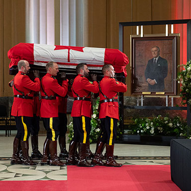 Eight uniformed members of the Royal Canadian Mounted Police carry a casket.
