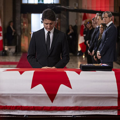 A man stands with his head bowed in front of a flag-draped casket.
