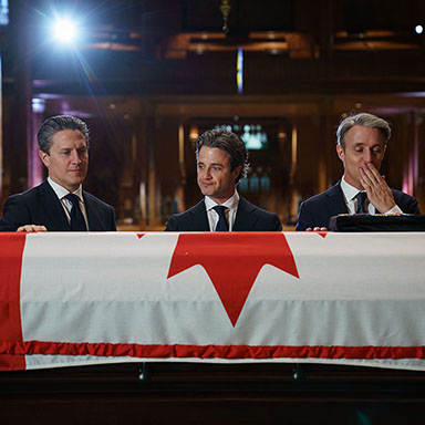 Three men stand in front of a flag-draped casket.
