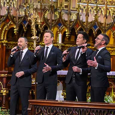 Four men stand and sing in a basilica.
